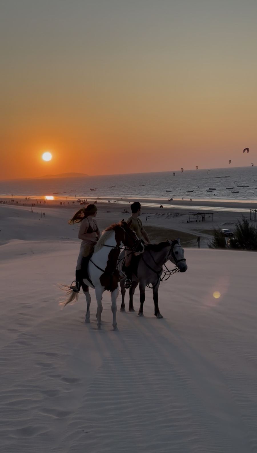 Cavaleiros parados no alto da duna da Barrinha, com o sol se pondo sobre o mar