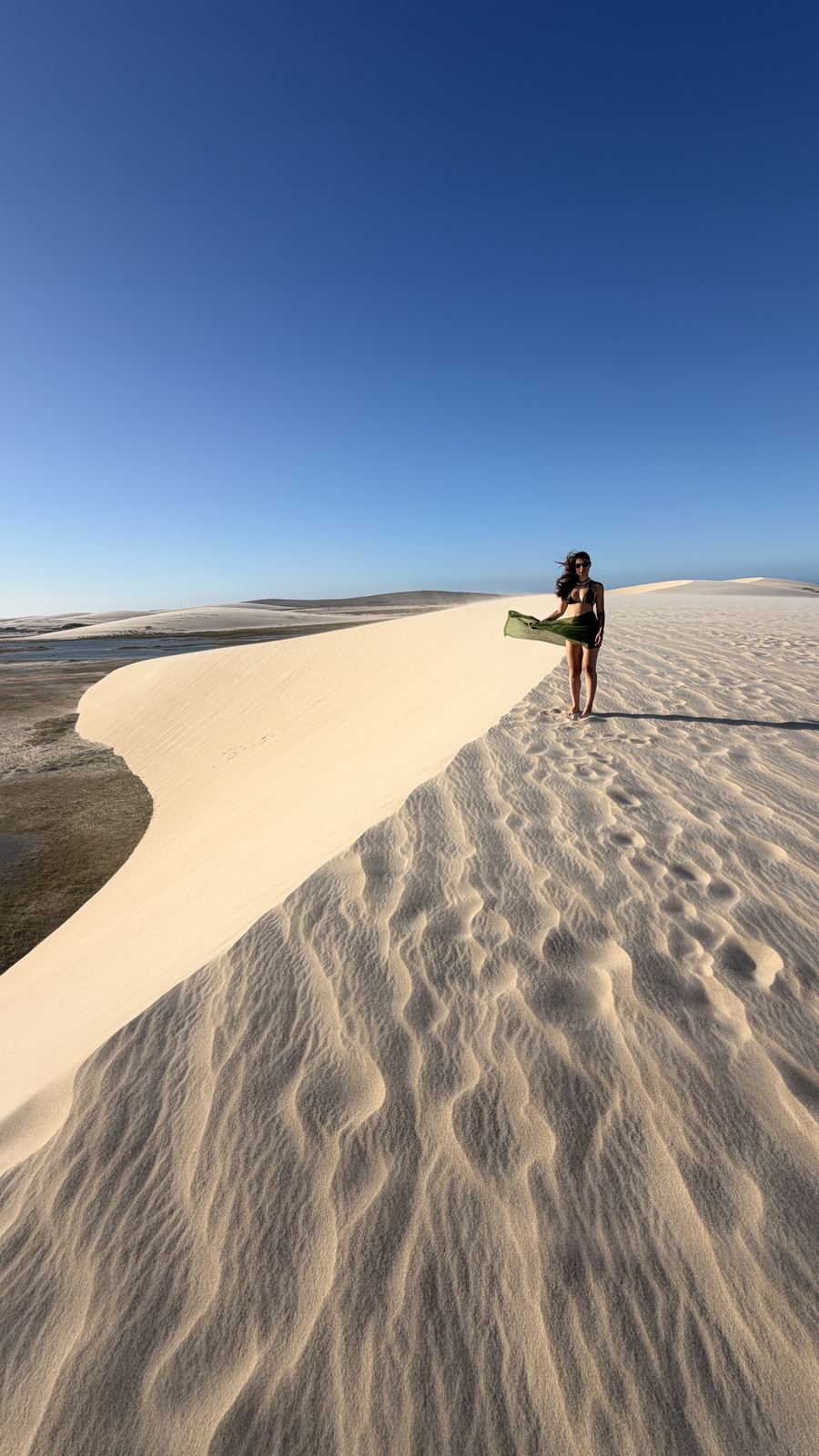 Lidiane Grigoletto no alto da duna da Lagoa do Amâncio no fim da tarde, com o vento levantando a saída de praia