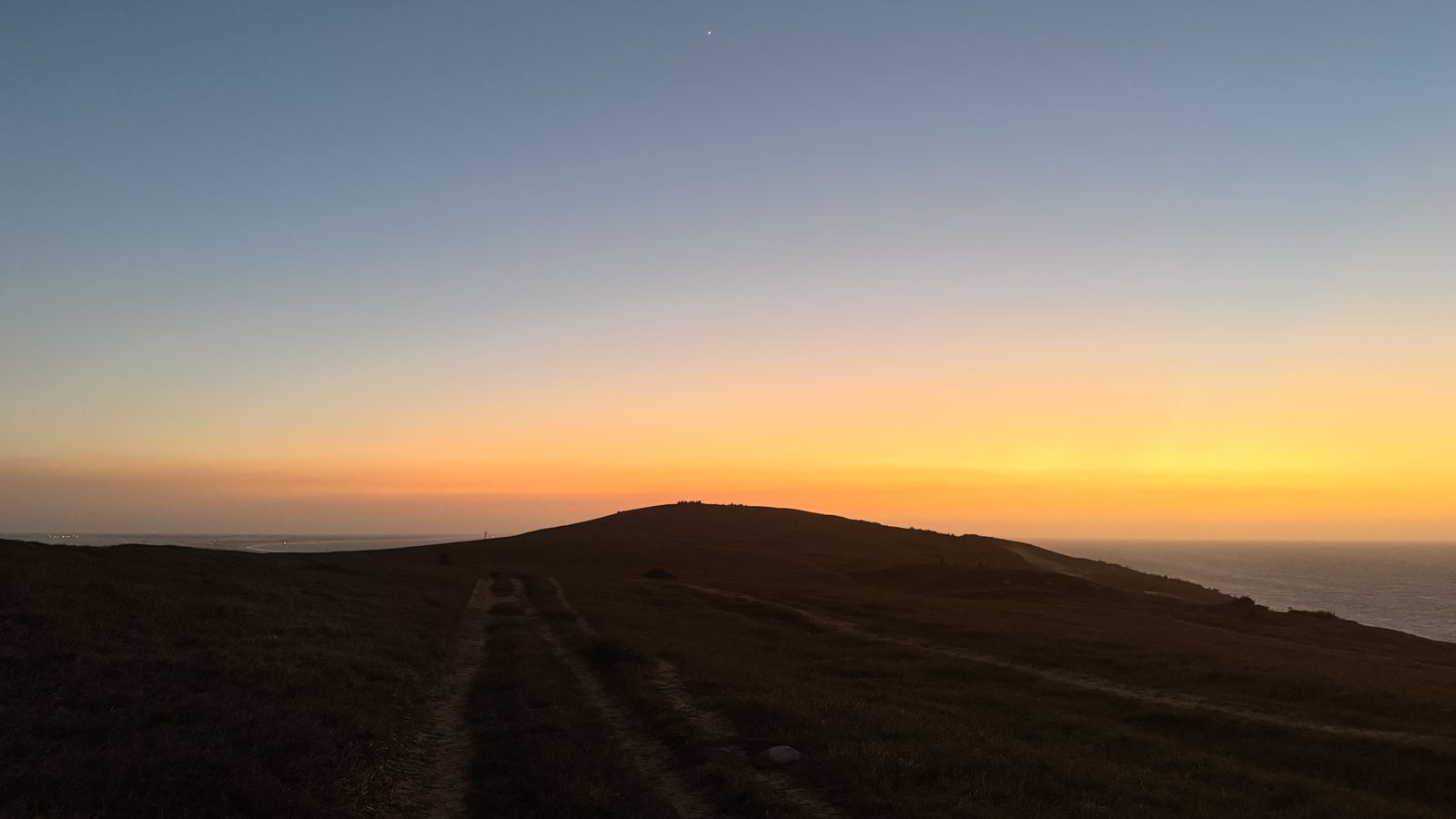 Morro do Serrote no entardecer, com o céu alaranjado e o mar ao fundo, na volta da Pedra Furada